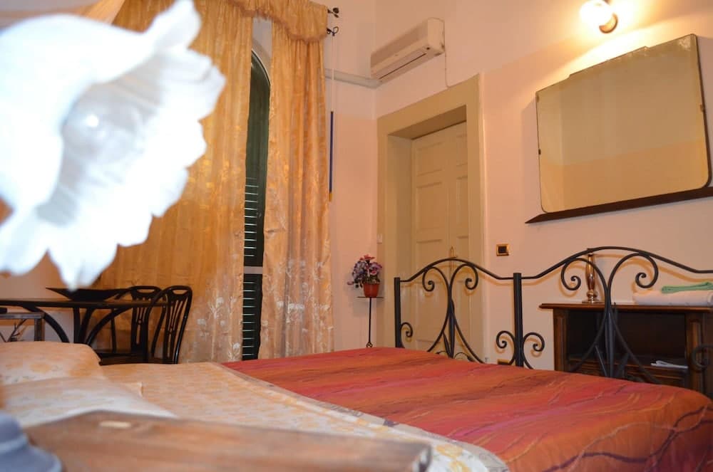 A cozy hotel room with twin beds adorned in warm-toned linens, a wrought iron headboard, and a quaint arched window framed by golden curtains, exudes a welcoming charm ideal for travelers seeking comfort and relaxation.