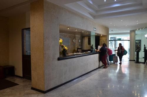 A modern hotel lobby features a sleek reception desk, polished marble floors, and travelers with luggage, creating a welcoming atmosphere ideal for business or leisure stays.