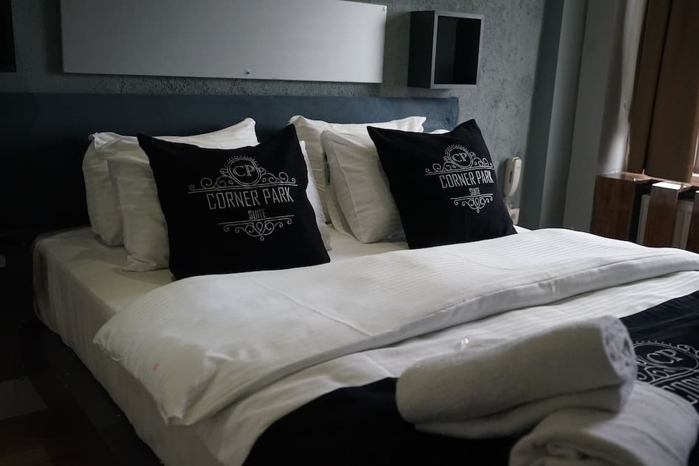 A cozy hotel suite features a neatly made bed adorned with branded pillows and towels, set against a modern wall design, ideal for travelers seeking comfort and style.