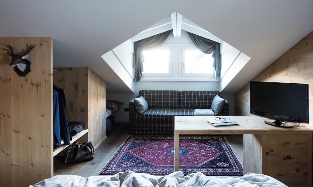 A cozy attic bedroom with wooden walls, a vibrant rug, and skylight windows creates a serene retreat perfect for travelers seeking a rustic and charming accommodation experience.