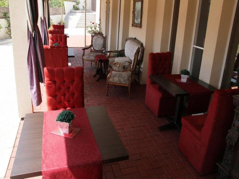 A cozy outdoor patio features vibrant red tufted chairs and tables adorned with greenery, creating an inviting atmosphere perfect for leisurely dining or relaxing in a charming café setting.