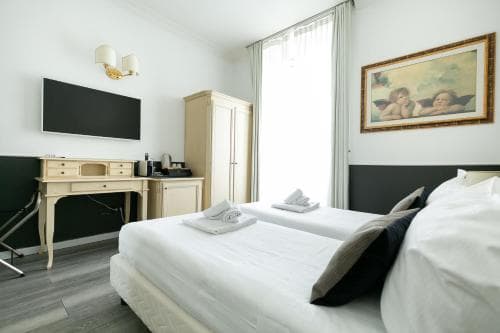 A cozy hotel room features a neatly made bed, vintage-style furniture, and soft natural light filtering through sheer curtains, creating an inviting atmosphere ideal for travelers seeking comfort and relaxation.