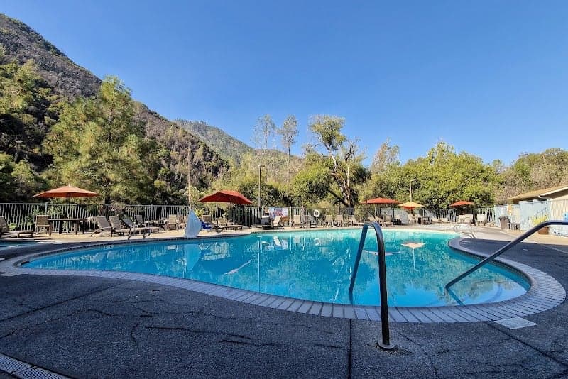 A serene outdoor pool surrounded by lush greenery and towering mountains offers a tranquil retreat at the Yosemite View Lodge, perfect for travelers seeking relaxation and natural beauty.