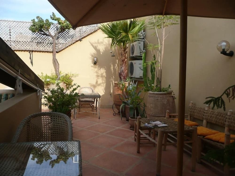 A serene courtyard patio features terracotta flooring, lush potted plants, wicker furniture, and a shaded seating area, ideal for travelers seeking a tranquil retreat in a warm climate destination.