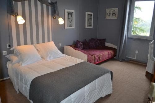 A cozy hotel room features a neatly made bed with white linens, a striped wall, and a window view of greenery, ideal for travelers seeking comfort and relaxation.