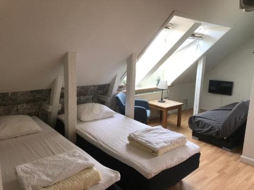 A cozy attic bedroom with slanted ceilings, twin beds neatly arranged with folded towels, a small desk by the window, and a relaxed atmosphere ideal for budget travelers seeking comfort.
