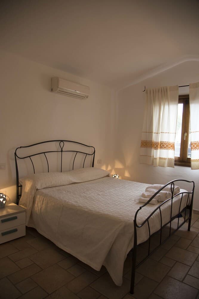 A cozy bedroom with a metal bed frame, tiled floor, and soft lighting creates a serene atmosphere, ideal for travelers seeking relaxation in a quaint accommodation.