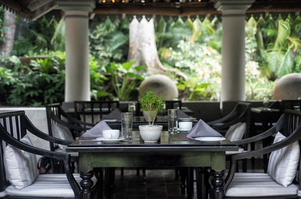 An elegant outdoor dining area with lush greenery and stone columns creates a serene tropical ambiance, perfect for travelers seeking a tranquil culinary experience.