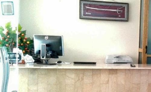 A cozy hotel reception area features a clean desk with a computer, framed sword decor, and vibrant orange tree accents, creating a welcoming atmosphere ideal for travelers seeking a comfortable stay.