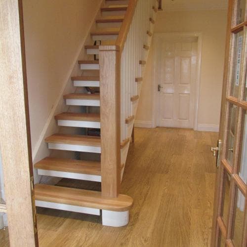A cozy indoor hallway featuring a wooden staircase with white risers, hardwood flooring, and a closed door, ideal for showcasing home interior design or renovation projects.