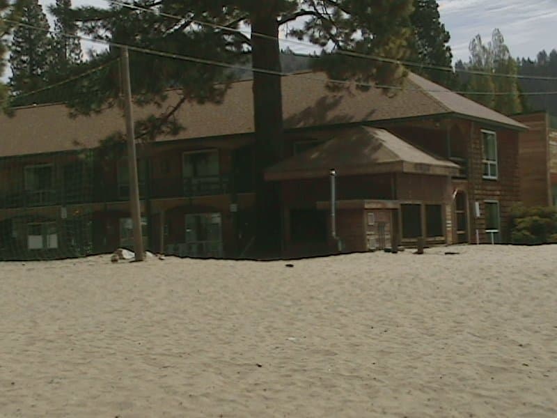 A serene lakeside lodge surrounded by sandy shores and towering pine trees offers a tranquil retreat for nature lovers seeking relaxation.