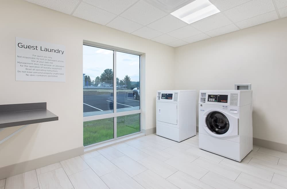 A bright, clean guest laundry room with white appliances, tiled floors, and large windows overlooking a parking lot, ideal for travelers needing convenient laundry facilities during their stay.