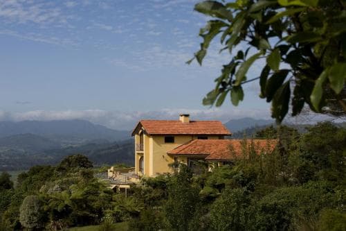 A serene countryside villa with terracotta roofs nestles amidst lush greenery under a partly cloudy sky, ideal for tranquil retreats and nature escapes.