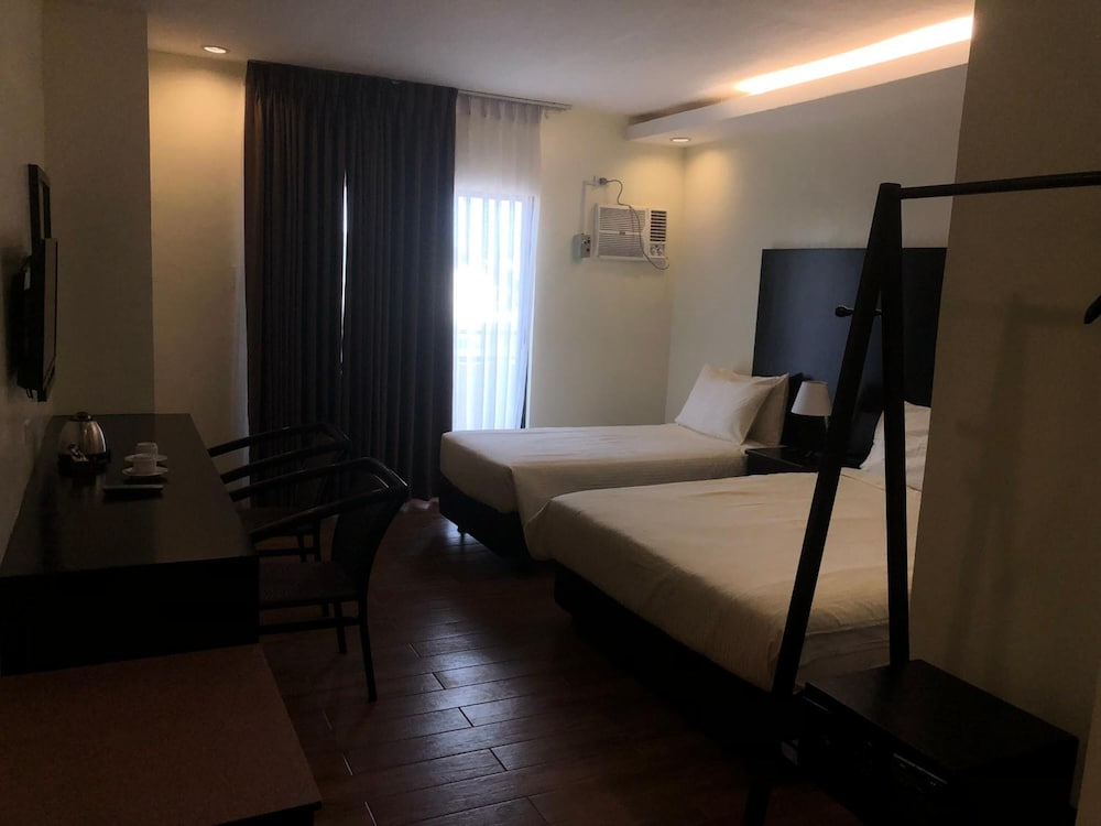 A cozy hotel room with two neatly made beds, a desk with chairs, a mounted TV, and soft lighting creates a welcoming atmosphere ideal for travelers seeking comfort and convenience.