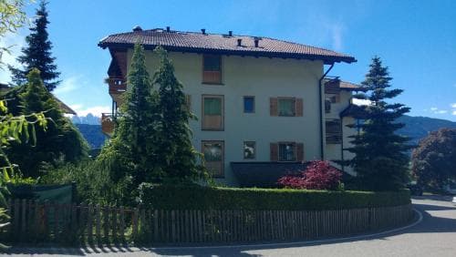 A serene mountain lodge surrounded by lush greenery and towering pines under a clear blue sky, ideal for tranquil alpine retreats.