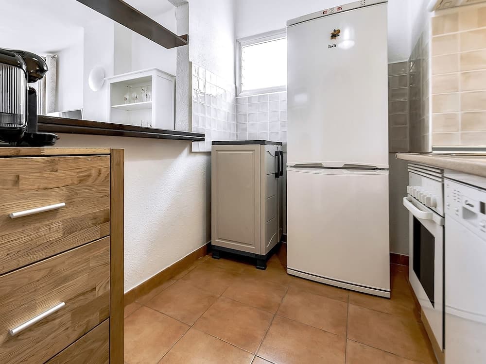 A cozy kitchen with wooden drawers, white appliances, tiled walls, and terracotta flooring offers a practical space for travelers seeking self-catering accommodations.