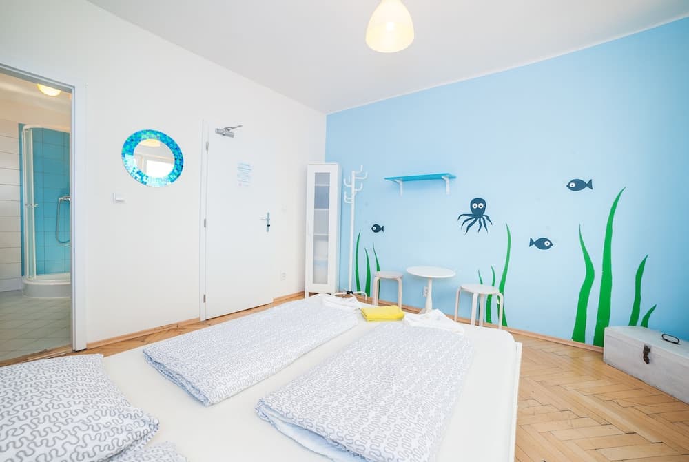 A cozy seaside-themed bedroom with blue walls adorned with ocean decals, neatly arranged bedding, and a visible shower area through a glass door, ideal for family-friendly beachside accommodations.