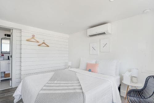 A cozy, minimalist bedroom with white shiplap walls, a neatly made bed, and modern furnishings creates a serene retreat ideal for travelers seeking relaxation in a boutique hotel setting.