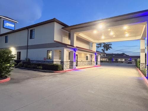 A warmly lit hotel entrance with purple accents invites travelers at dusk, featuring a covered driveway and modern architecture ideal for a comfortable stay.