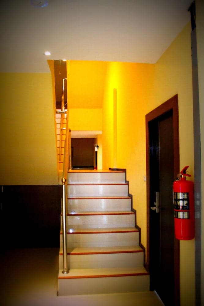 A warmly lit indoor staircase with yellow walls, wooden steps, a polished railing, and a red fire extinguisher creates an inviting atmosphere ideal for travelers exploring cozy accommodations.