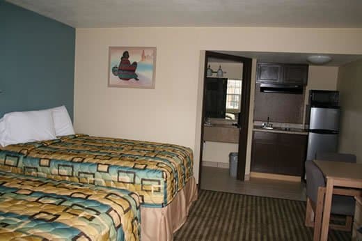 A cozy motel room features two patterned beds, a compact kitchenette with a refrigerator and microwave, and a warm, inviting atmosphere ideal for travelers seeking comfort and convenience.