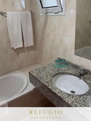 A cozy hotel bathroom features a granite countertop sink, a bathtub, neatly hung towels, and a small window, creating a serene and inviting atmosphere ideal for travelers seeking comfort and relaxation.