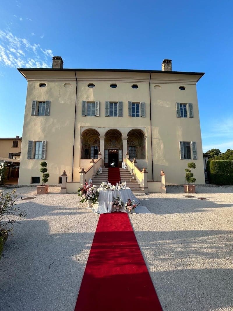 A picturesque Italian villa with a grand staircase adorned by a red carpet leads to an elegant entrance, perfect for luxurious events and romantic getaways under a serene blue sky.