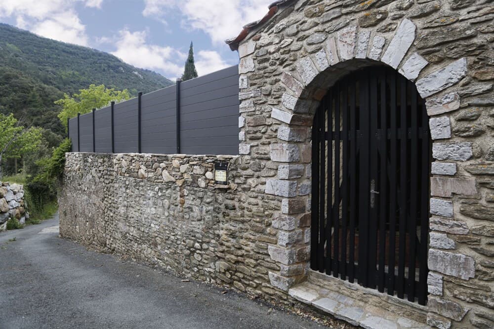 A serene rural scene features a rustic stone wall with an arched gate, set against lush green hills under a partly cloudy sky, ideal for travelers seeking peaceful countryside retreats.