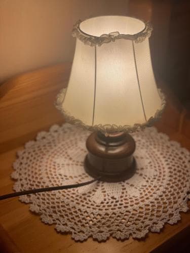 A cozy table lamp with a lace-trimmed shade casts warm light over a delicate crocheted doily, creating an inviting atmosphere perfect for a relaxing evening at home or a quaint bed and breakfast setting.