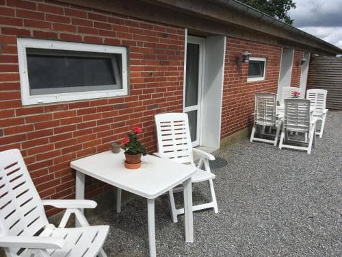 A cozy brick cottage patio features white outdoor furniture and a potted flower, creating a serene and inviting atmosphere ideal for a relaxing getaway.