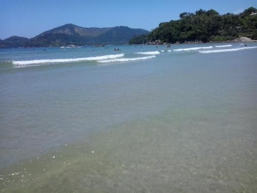 A serene tropical beach scene with clear turquoise waters, gentle waves, lush green hills in the background, and scattered beachgoers enjoying the sunny day, ideal for relaxation and coastal exploration.