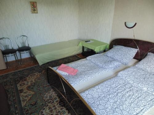 A cozy budget hotel room features twin beds with patterned linens, a small table with chairs, and a warm rug, ideal for travelers seeking simple accommodations.