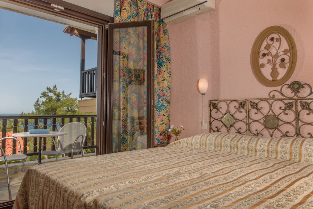 A cozy hotel room with a patterned bedspread, ornate iron headboard, and vibrant curtains opens to a serene balcony view, perfect for travelers seeking relaxation and comfort.