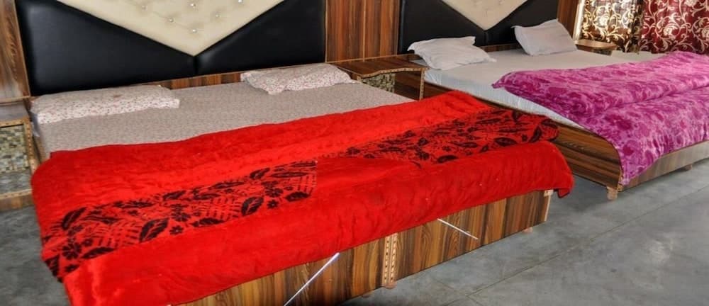 A cozy hotel room features two neatly arranged beds with vibrant red and purple blankets, wooden furnishings, and a warm ambiance, ideal for travelers seeking comfort and relaxation.