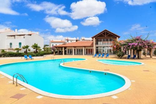 A vibrant resort scene featuring a sparkling blue pool surrounded by lounge chairs under a sunny sky, ideal for family vacations seeking relaxation and leisure.