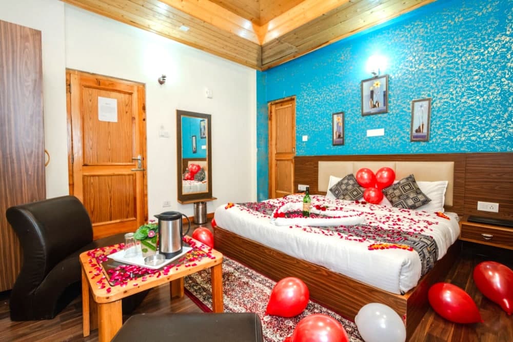 A cozy hotel room with vibrant blue walls, wooden accents, and romantic decorations like rose petals and balloons, perfect for a special getaway or honeymoon stay.