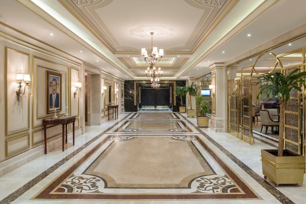A luxurious hotel lobby features ornate marble floors, golden accents, elegant chandeliers, and framed portraits, creating an opulent atmosphere ideal for high-end travelers seeking premium accommodations.