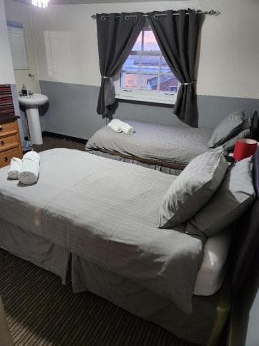 A cozy budget-friendly hotel room features neatly made beds with gray linens, a window with curtains offering a city view, and basic amenities like a sink and towels, ideal for travelers seeking simple accommodations.