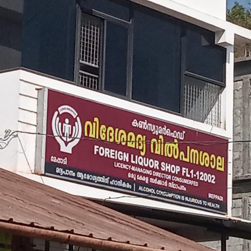 A vibrant red signboard marks the ConsumerFed Foreign Liquor Shop in Meppadi, Kerala, inviting travelers to explore local beverage options amidst a bustling urban setting.