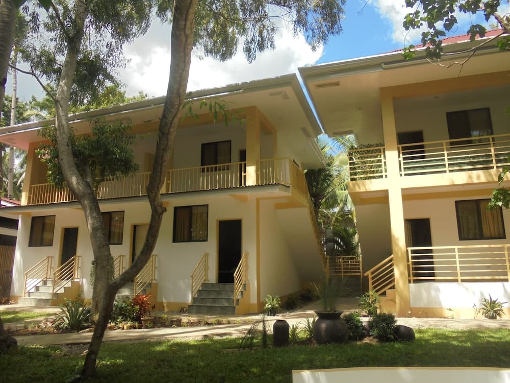 A serene tropical resort features pastel-colored buildings with balconies surrounded by lush greenery, ideal for vacationers seeking a peaceful retreat.