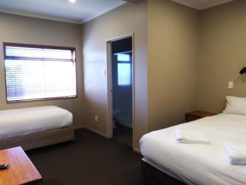 A cozy hotel room with two neatly made beds, a small wooden table, and a window with blinds, offering a simple and inviting atmosphere ideal for travelers seeking restful accommodations.