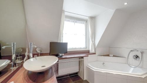 A cozy attic bathroom with a sloped ceiling features a modern sink, bathtub, and TV, creating a serene retreat ideal for travelers seeking relaxation and comfort.