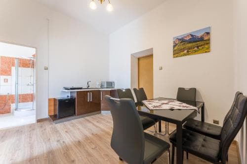A cozy apartment interior features a modern kitchenette, dining area with a patterned tablecloth, and a scenic mountain artwork, ideal for travelers seeking a comfortable self-catering stay.