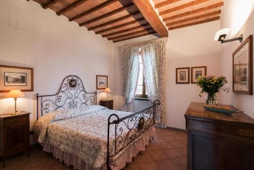 A cozy bedroom with rustic wooden beams, floral curtains, and antique furnishings exudes warmth and charm, ideal for travelers seeking a serene retreat in a historic villa.