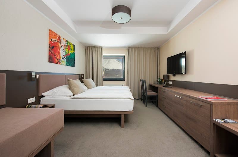 A cozy hotel room at the Hotel Panorama Resort in Štrbské Pleso, Slovakia, features modern furnishings, a scenic mountain view through the window, and a warm, inviting atmosphere ideal for travelers seeking relaxation and comfort.