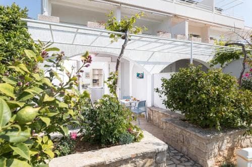 A serene courtyard garden with lush greenery and vibrant flowers frames a cozy seating area outside a charming apartment complex, ideal for travelers seeking a peaceful retreat.