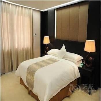 A cozy hotel room features a neatly made bed with white linens, soft lighting from bedside lamps, and elegant curtains, creating a serene atmosphere ideal for travelers seeking relaxation.