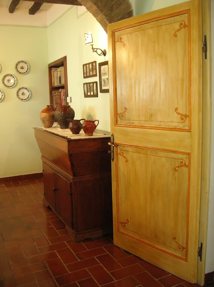 A cozy, rustic interior features terracotta flooring, a wooden cabinet adorned with pottery, decorative plates on the wall, and a charming arched doorway, ideal for travelers seeking traditional European ambiance in their accommodations.