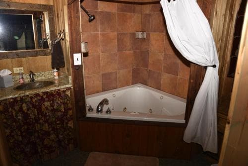 A cozy cabin bathroom features a tiled corner jacuzzi tub, rustic wooden accents, and a floral-patterned vanity, creating a serene retreat ideal for travelers seeking relaxation.