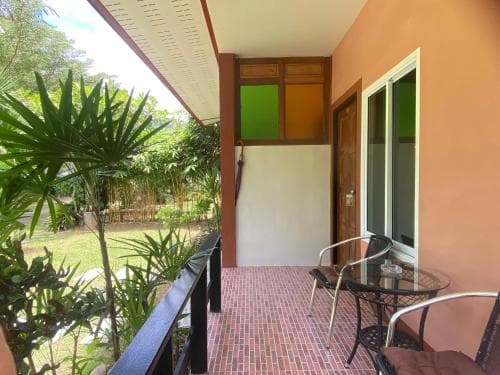 A cozy balcony with brick flooring, glass table, chairs, and lush greenery overlooks a tranquil garden, ideal for a peaceful retreat or vacation rental listing.